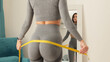 © shevtsovy - Fitness Woman Measuring butt With Tape at home. strong buttocks concept. Beautiful woman checking success of weight loss program and measuring butt and hips in front of mirror in living room.