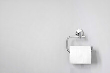 Chrome Toilet Paper Holder On White Wall Holding A Roll Of Soft Bath Tissue. Design Element And Copy Space.