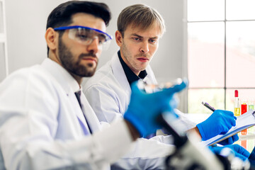 Professional two scientist man research and working doing a chemical experiment while making analyzing and mixing liquid in test tube.Young science man dropping sample chemical on glass at laboratory