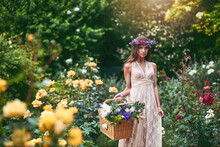 Her Basket Is Blooming With Variety. Shot Of A Beautiful Young Woman Wearing A Floral Head Wreath And Holding A Basket Full Of Flowers In Nature.