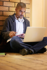 Wall Mural - Hes got all his notes saved online. Shot of a college student using his laptop while sitting in a hallway at campus.