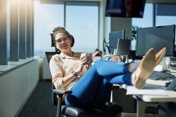 Poster - Work is so laid back today. Shot of a cheerful young businesswoman drinking coffee while sitting with her feet up on her desk inside of the office.