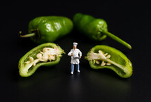 Miniature Chef Standing With Green Peppers On Black Background