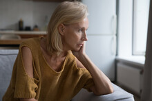 Depressed Mature Blonde Lady Looking At Window Away With Unhappy, Frustrated, Disappointed Stare, Thinking Over Health Disability, Loneliness. Sad Frustrated Woman Home Candid Portrait