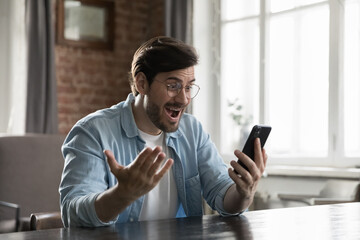 Wall Mural - excited smartphone user man staring at screen in surprise, reading text message getting good news, r