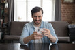 © fizkes - Happy cheerful freelance business professional using online app on smartphone at home office work table, reading text message, typing, chatting on internet, making video call, getting good news