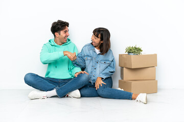 Wall Mural - Young couple making a move while picking up a box full of things sitting on the floor isolated on white background handshaking after good deal