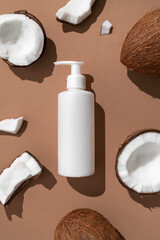 Wall Mural - White cosmetic bottles, broken fresh coconut with sunny contrast shadows on brown background top view. Organic natural cosmetics with coconut oil. Plastic packaging products for branding, mock up