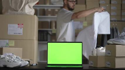 Wall Mural - Laptop with blank green screen standing on the desktop in the warehouses. Asian man online seller checking stock and Inventory before sending to the customer.