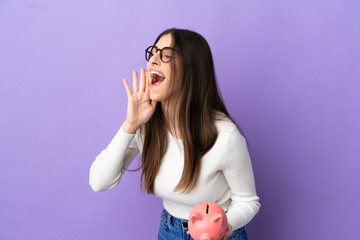 Wall Mural - Young caucasian woman holding a piggybank isolated on purple background shouting with mouth wide open to the side