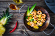 Fried prawns and pineapple in frying pan on wooden table
