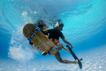 Man and Woman skateboarding underwater in the swimming pool.