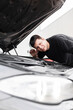 © alones - Man driver stands the car with the hood open and checks the sound of the engine. Professional mechanic guy checks the car and listens