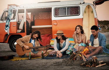 We come together and have fun. Shot of a group of friends sitting around a fire on the beach.