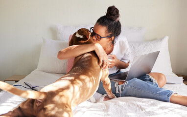 Mama says chocolates bad but I can have her kisses. Shot of a beautiful young woman using a laptop while relaxing with her dog in bed at home.