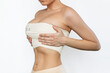 Cropped shot of young fit woman wrapped in elastic bandage after breast augmentation isolated on white background. Result of lifting. Pain after plastic surgery. Girl is trying to hide her big breast