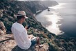 © panophotograph - Digital nomad, man in the hat, a businessman with a laptop sits on the rocks by the sea during sunset, makes a business transaction online from a distance. Remote work on vacation.