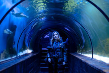 Woman In The Aquarium. Tourist On An Excursion In An Underwater Tunnel With Fish.