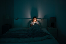 Sleepy Exhausted Woman Lying In Bed Using Smartphone, Can Not Sleep. Insomnia, Addiction Concept. Sad Girl Bored In Bed Scrolling Through Social Networks On Mobile Phone Late At Night In Dark Bedroom.