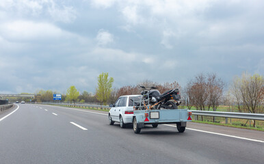 White car driving on highway with trailer holding motorcycle