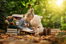 Reading Takes Us Somewhere Else. Shot Of A Little Girl Reading To Her Toys While Out In The Woods.
