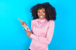 © Jihan - young woman with afro hairstyle in technical sports shirt against blue background points at copy space indicates for advertising gives right direction