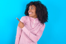 Young Woman With Afro Hairstyle In Technical Sports Shirt Against Blue Background Glad Cheery Demonstrating Copy Space Look Novelty
