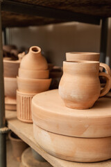 Shelves with bowls, plates, jars, teapots, etc. made in clay in natural raw color until the final painting. Crafts in clay.