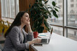 © ARUTA Images - Smiling successful businesswoman using laptop computer planning project looking at window in modern office. Portrait of young confident secretary sitting at workplace