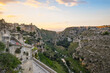 Tourists enjoy late afternoon views of the ancient sassi caves and gravina ravine from an outdoor cafe patio in the city of Matera, Italy.