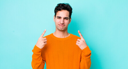 Poster - handsome hispanic man with a bad attitude looking proud and aggressive, pointing upwards or making fun sign with hands