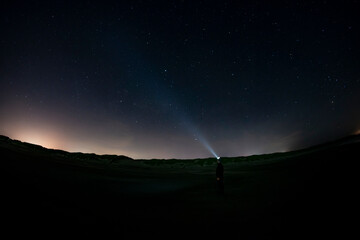 Adventurous man watching the stars on a beach at night with his headlamp shinning up at the stars.