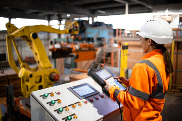 Wall Mural - Female worker in safety equipment and hardhat controlling parts assembling in factory. Industrial machines working in background.