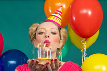 Beautiful Young Woman Wearing Party Hat Blowing Candles On Birthday Cake Against Green Background