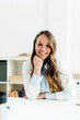 © Westend61 - Happy businesswoman with hand on chin at desk in office