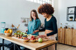 © Westend61 - Smiling young woman cutting strawberries by friend eating apple at table in kitchen