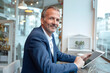 © Westend61 - Smiling businessman sitting at table by glass window with tablet PC