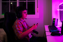 Boy With Game Controller Sitting On Chair In Bedroom At Home
