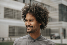 Smiling Young Man With Curly Hair In Front Of Modern Building