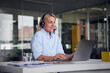 © Westend61 - Smiling businesswoman wearing headset using laptop at desk in office