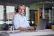© Westend61 - Smiling businesswoman wearing headset and laptop at desk in office