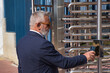 Mature, executive, gray-haired man with beard, sunglasses and jacket, showing a code with his cell phone to a reader at the entrance of the company. Concept qr codes, readers, fingerprints, security.