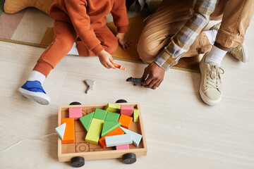 Wall Mural - Top view closeup of black father and son playing with wooden toys together sitting on floor in kids room, copy space