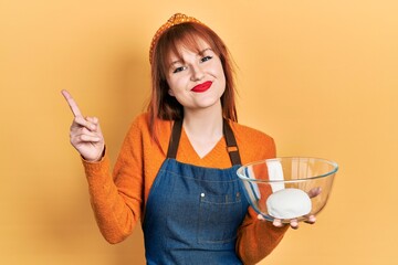 Sticker - Redhead young woman holding bread dough smiling happy pointing with hand and finger to the side