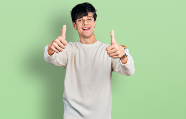 Handsome hipster young man wearing casual winter sweater approving doing positive gesture with hand, thumbs up smiling and happy for success. winner gesture.