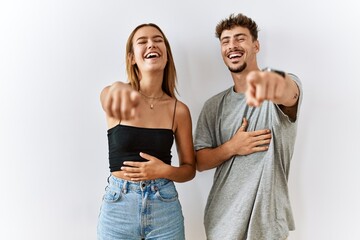 Sticker - Young beautiful couple standing together over isolated background laughing at you, pointing finger to the camera with hand over body, shame expression