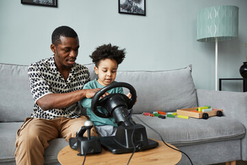 Wall Mural - Portrait of black father and son playing racing games on PC with steering wheel, copy space