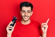© Krakenimages.com - Young hispanic man holding electric razor machine smiling happy pointing with hand and finger to the side