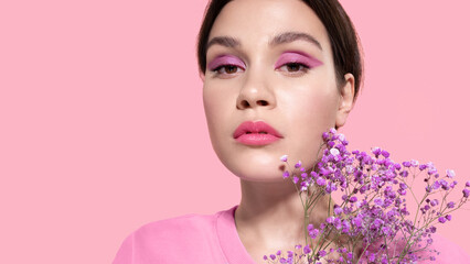 Wall Mural - Pretty  girl with pink makeup eyeshadow, lilac spring flowers, healthy smooth skin, fresh beautiful complexion on pink studio background. Womens day holiday, natural woman beauty concept.