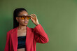 Fashionable elegant Black woman wearing trendy sunglasses with leopard frame, yellow glass, orange blazer, posing on green background. Copy, empty space for text